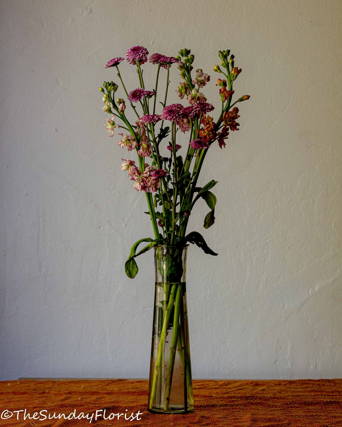 Drying bouquet in glass vase against cream wall